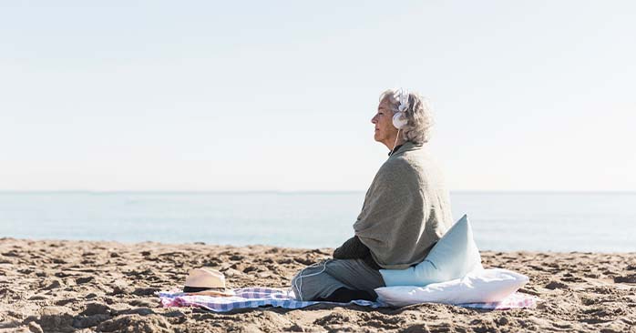 Woman meditating on the beach wearing headphones.